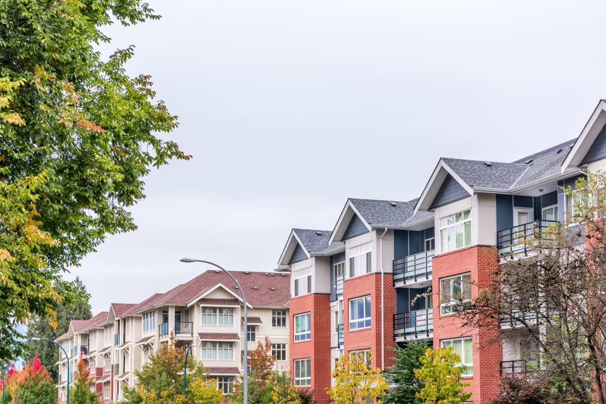 Row of modern multifamily residential buildings with brick facades and a tree-lined street