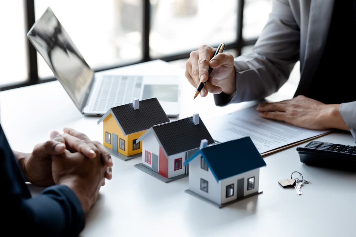 Real estate agent presenting property options to a client with miniature house models and documents on a meeting table