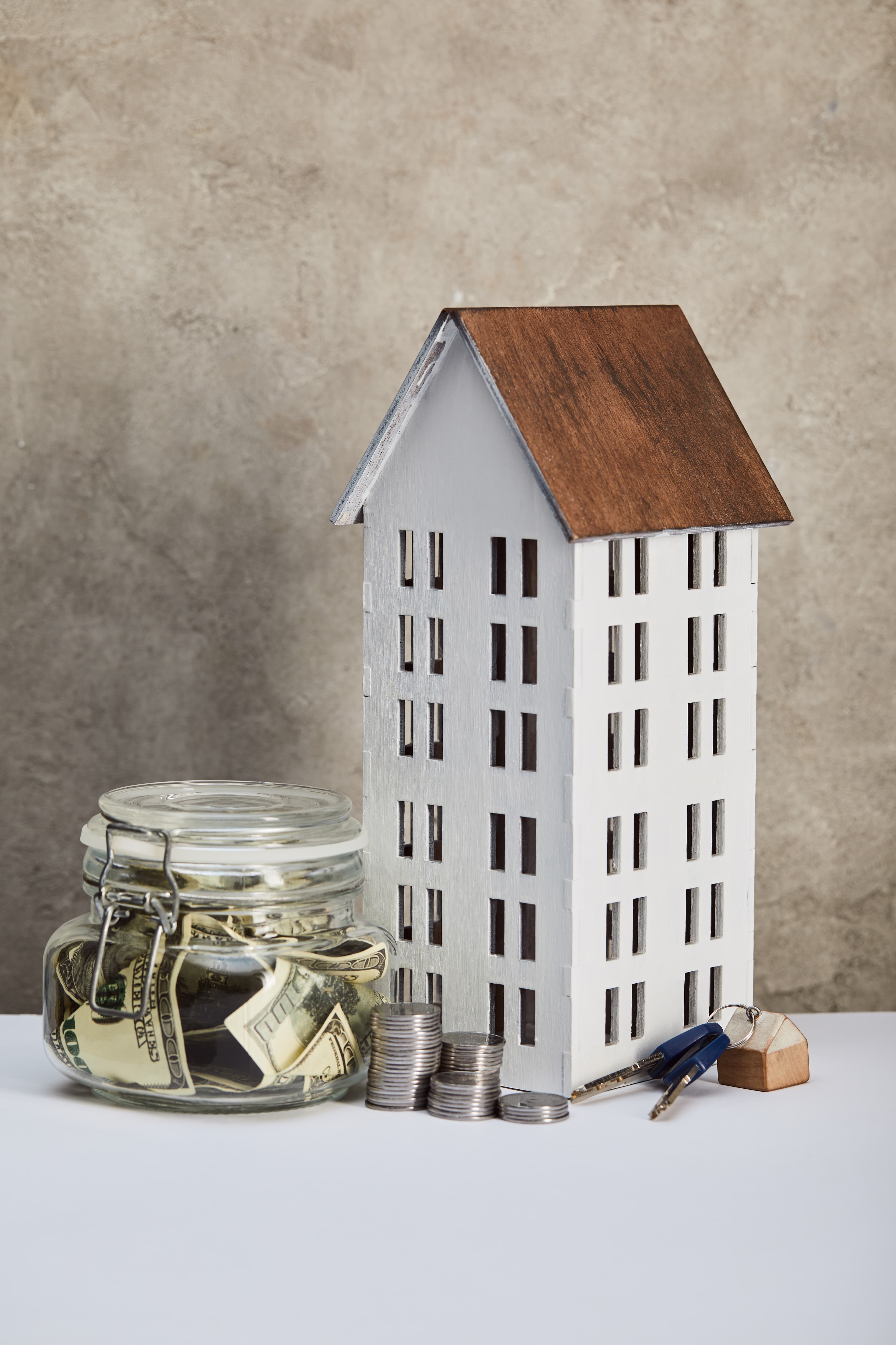 Decorative model of a multi-story building next to a glass jar of coins and property keys on a table
